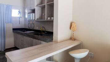 Cocina compacta con microondas, un lavamanos y un taburete pequeño.