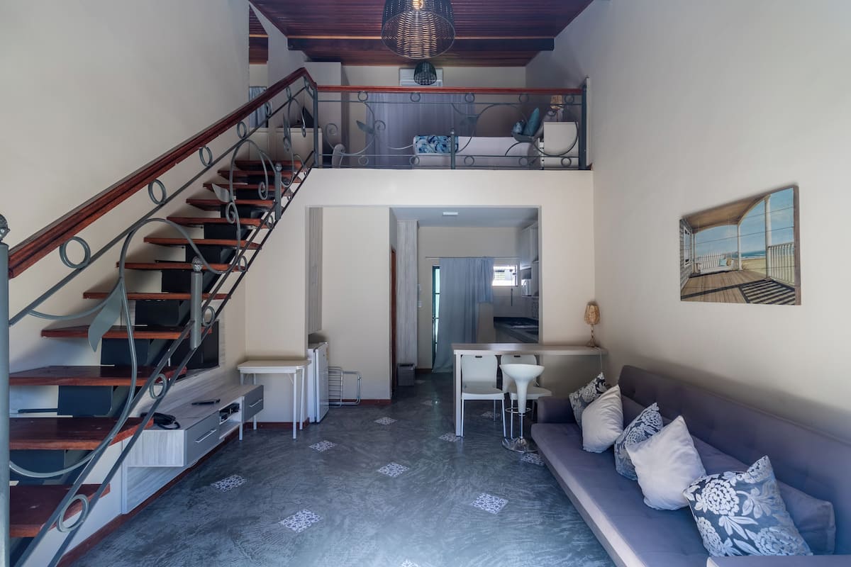 A spacious living area with a staircase, a dining area, and a sofa with cushions.