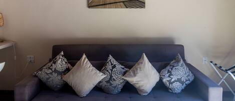 A modern living room with a grey sofa, patterned cushions, a wall-mounted artwork of a beach scene, and a patterned rug.