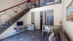 A modern living room with a staircase, a flat-screen TV, a dining area, and a sofa.