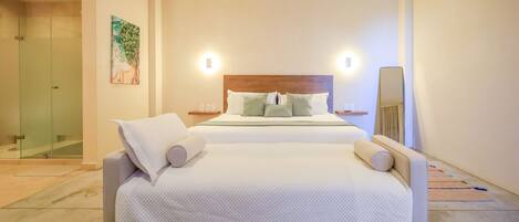A modern bedroom with a large bed, a nightstand, a wall-mounted mirror, and a glass shower enclosure.