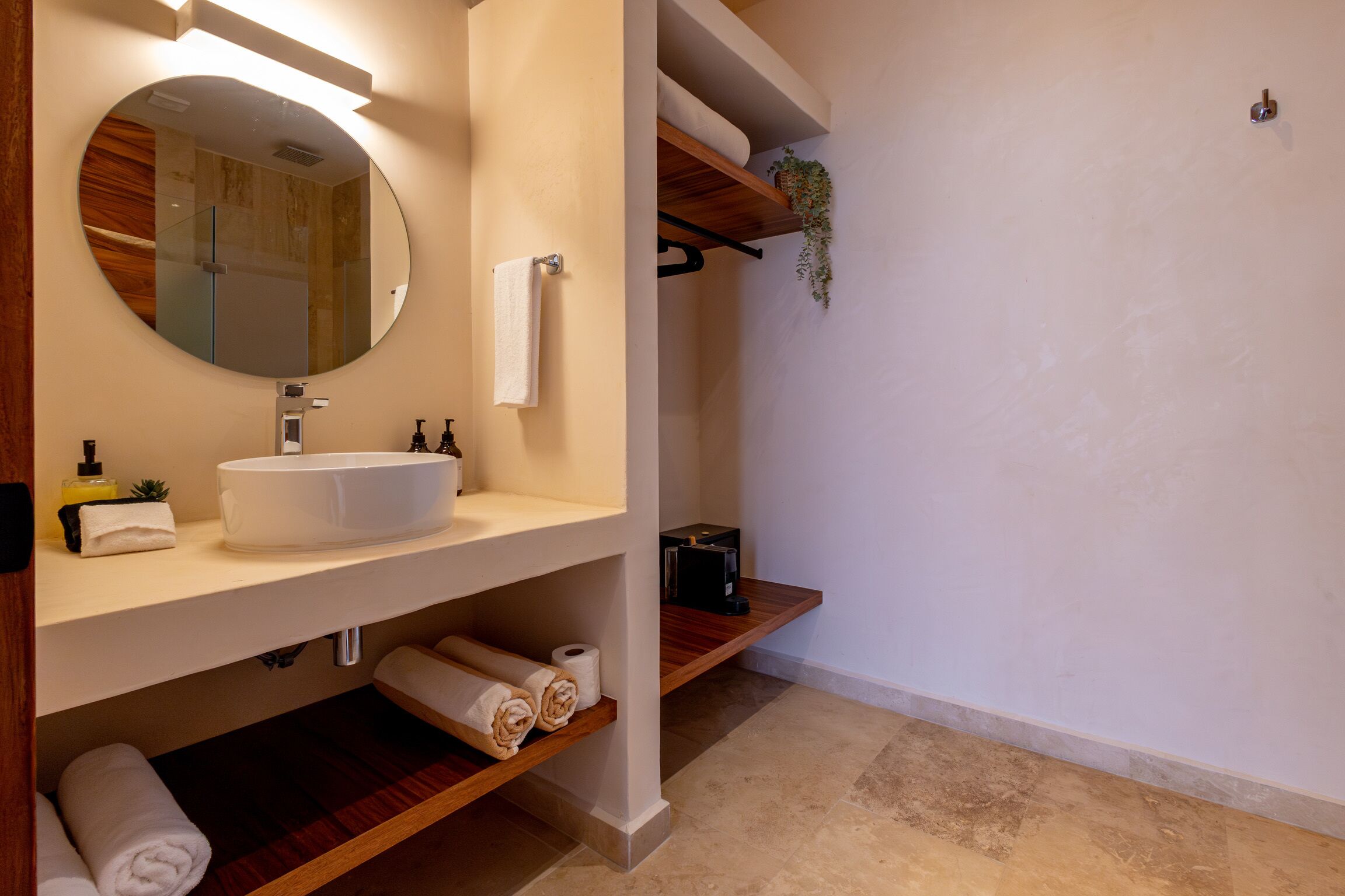 Un baño moderno con un espejo redondo, lavabo blanco y estantes de madera.