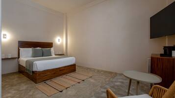 Un dormitorio moderno con una cama de madera, lámparas de noche, una mesita redonda y un televisor montado en la pared.