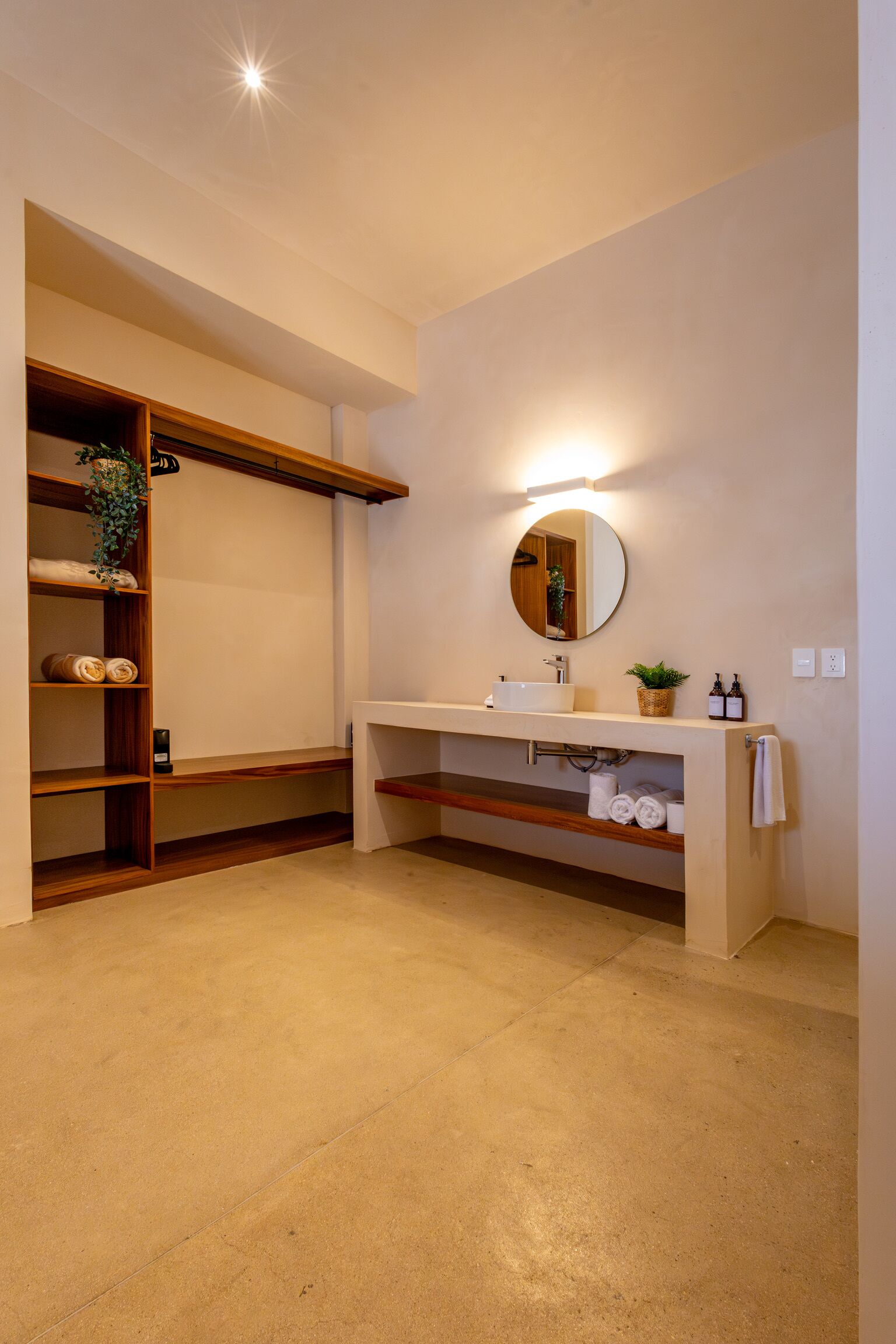 Ein modernes Badezimmer mit einer eingebauten Regaleinheit, einem runden Spiegel und einem weißen Waschbecken.
