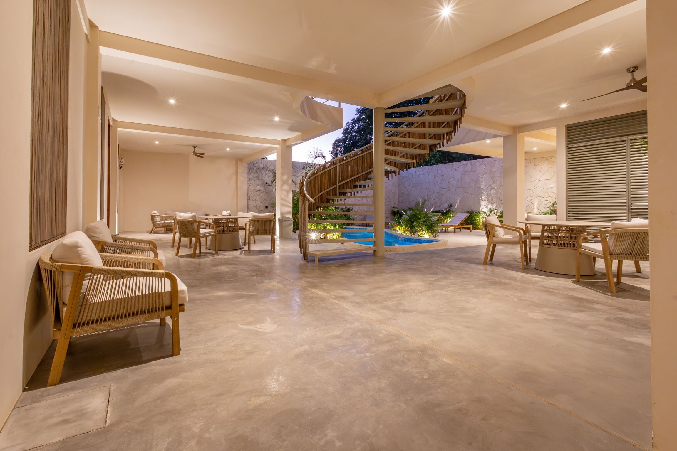 Un espacio interior amplio con una escalera en espiral, zonas de estar y un área de piscina.