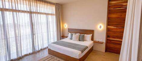 A bedroom with a large bed, a ceiling fan, a wooden wardrobe, and a window with sheer curtains.