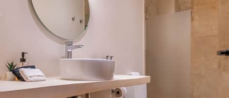 Ein modernes Badezimmer mit rundem Spiegel, weißem Waschbecken und einer Duschkabine aus Glas.
