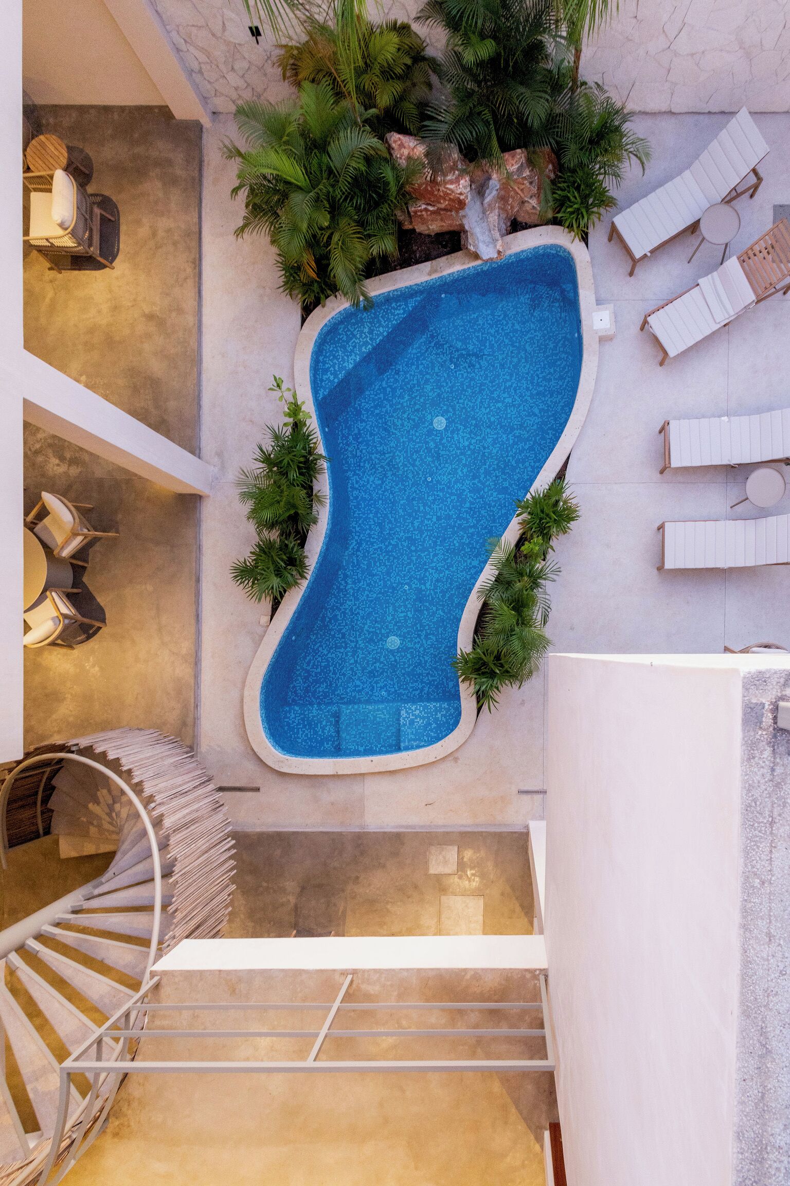 Une piscine intérieure moderne à la forme originale, entourée de chaises longues et de verdure.