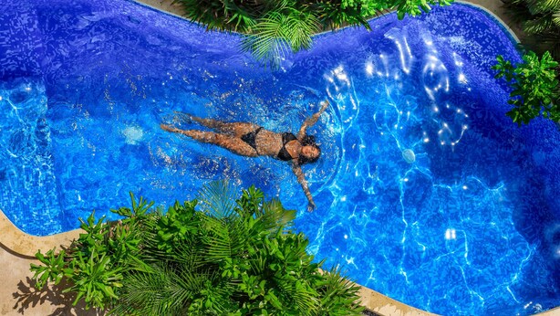 A person swimming in a blue pool surrounded by green plants. - Hotel Manglar  (Puerto Escondido)