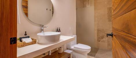 A modern bathroom with a round mirror, white sink, and a glass-enclosed shower.