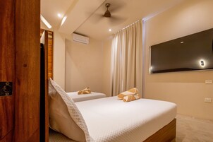 Habitación de hotel con dos camas, ventilador de techo, aire acondicionado y televisor de pantalla plana montado en la pared.