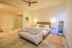 Un dormitorio moderno con cama, sofá, bañera y un espejo grande.