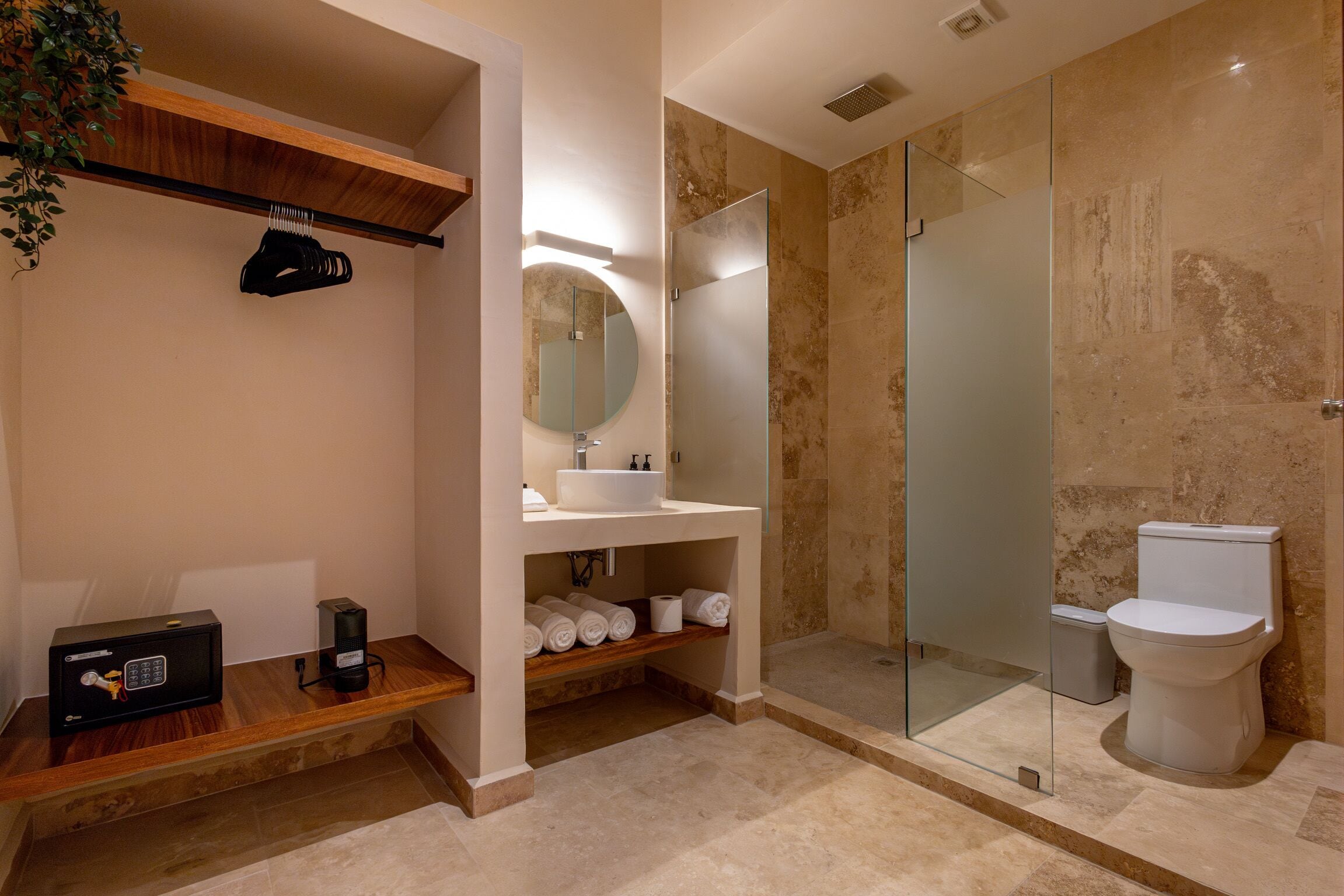 A modern bathroom with a glass-enclosed shower, a wooden vanity, a round mirror, and a toilet.