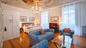 A spacious room with a large bed, a blue sofa, a glass coffee table, and a chandelier. - Once Upon Lisboa (Lisbon)