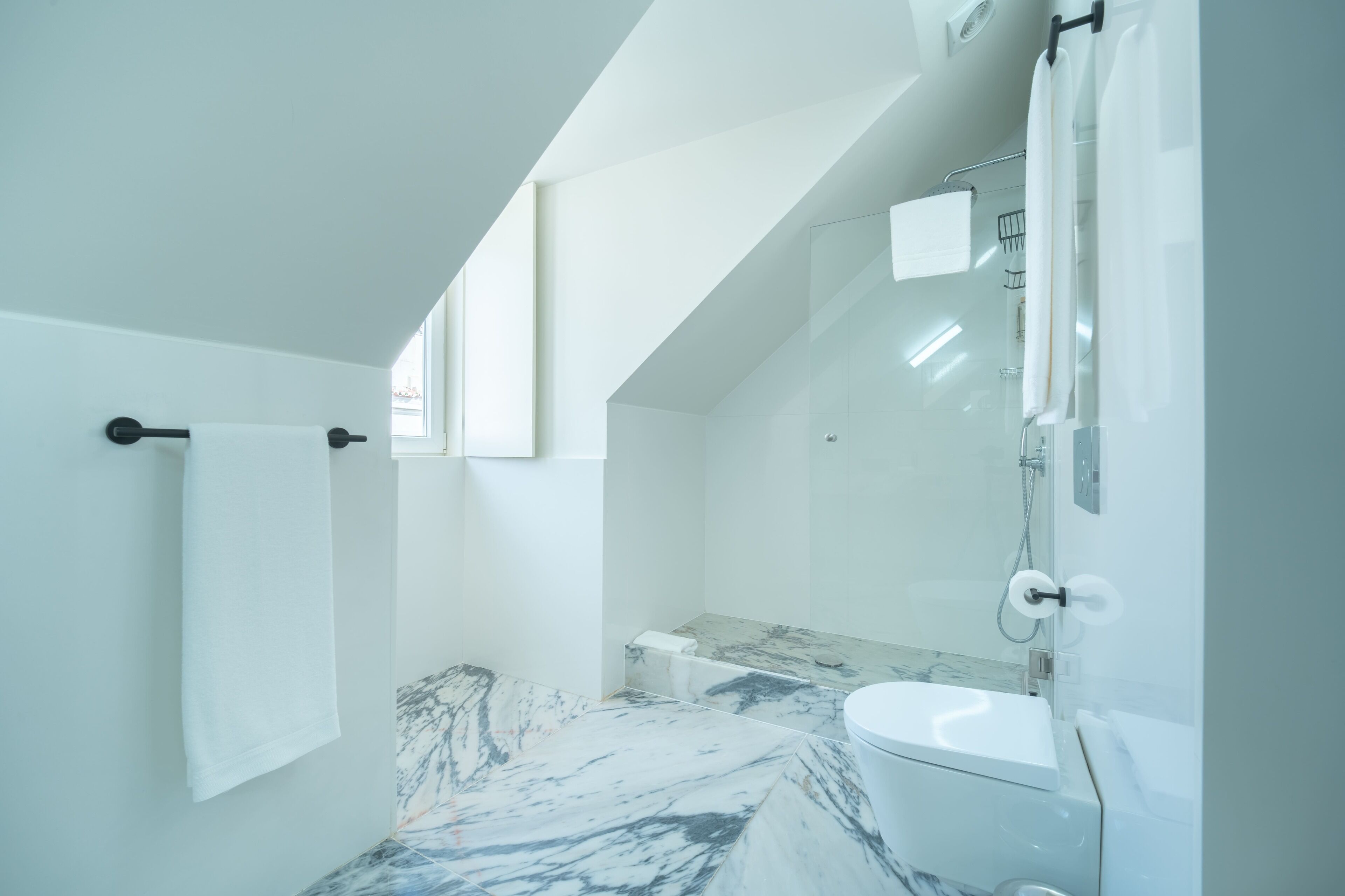 Un baño moderno con suelo de mármol, inodoro, ducha y toallero.