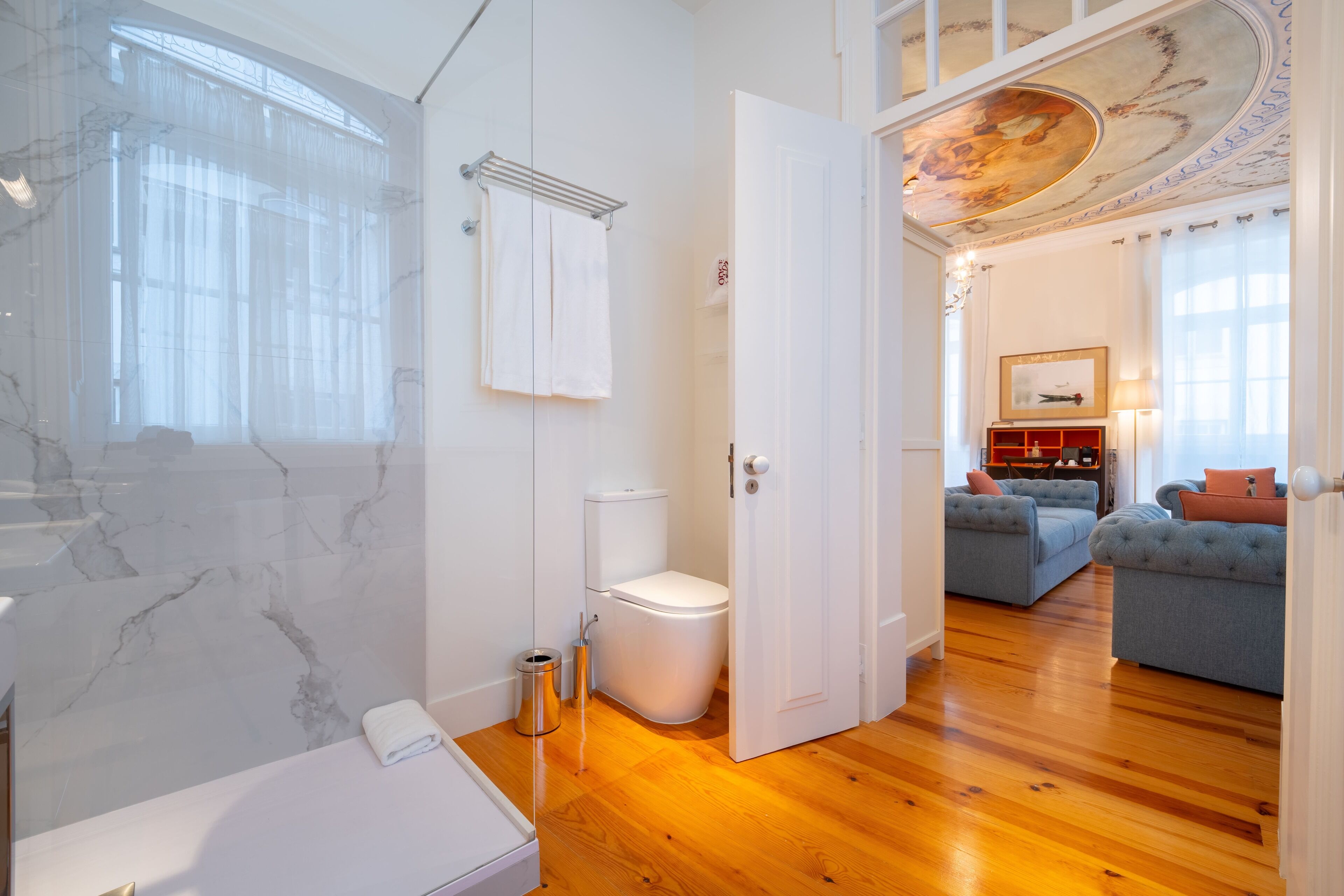 Un bagno con parete in marmo, un water bianco, zona doccia e pavimento in legno.