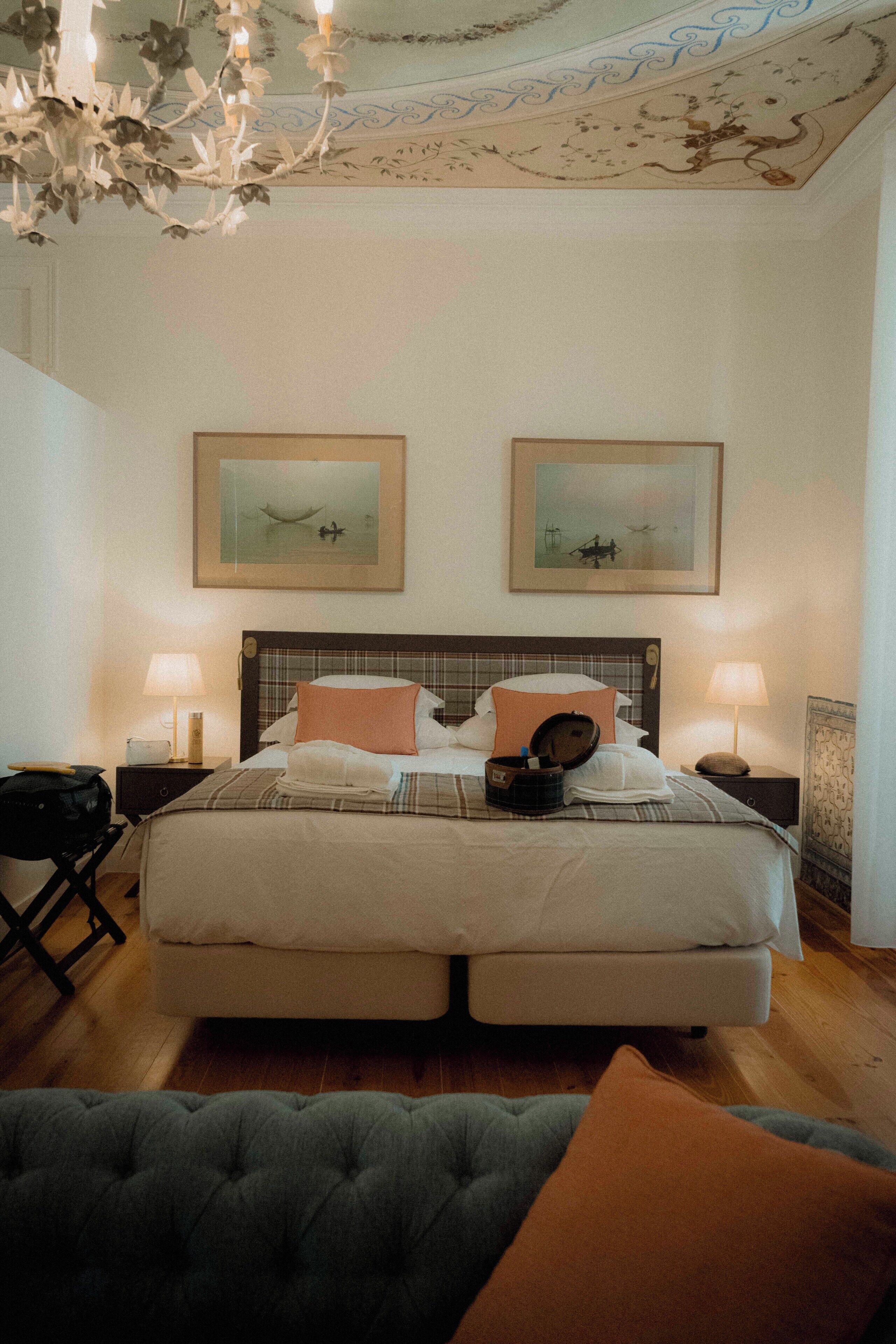 A double bed with a plaid headboard, two bedside lamps, and two framed artworks on the wall.