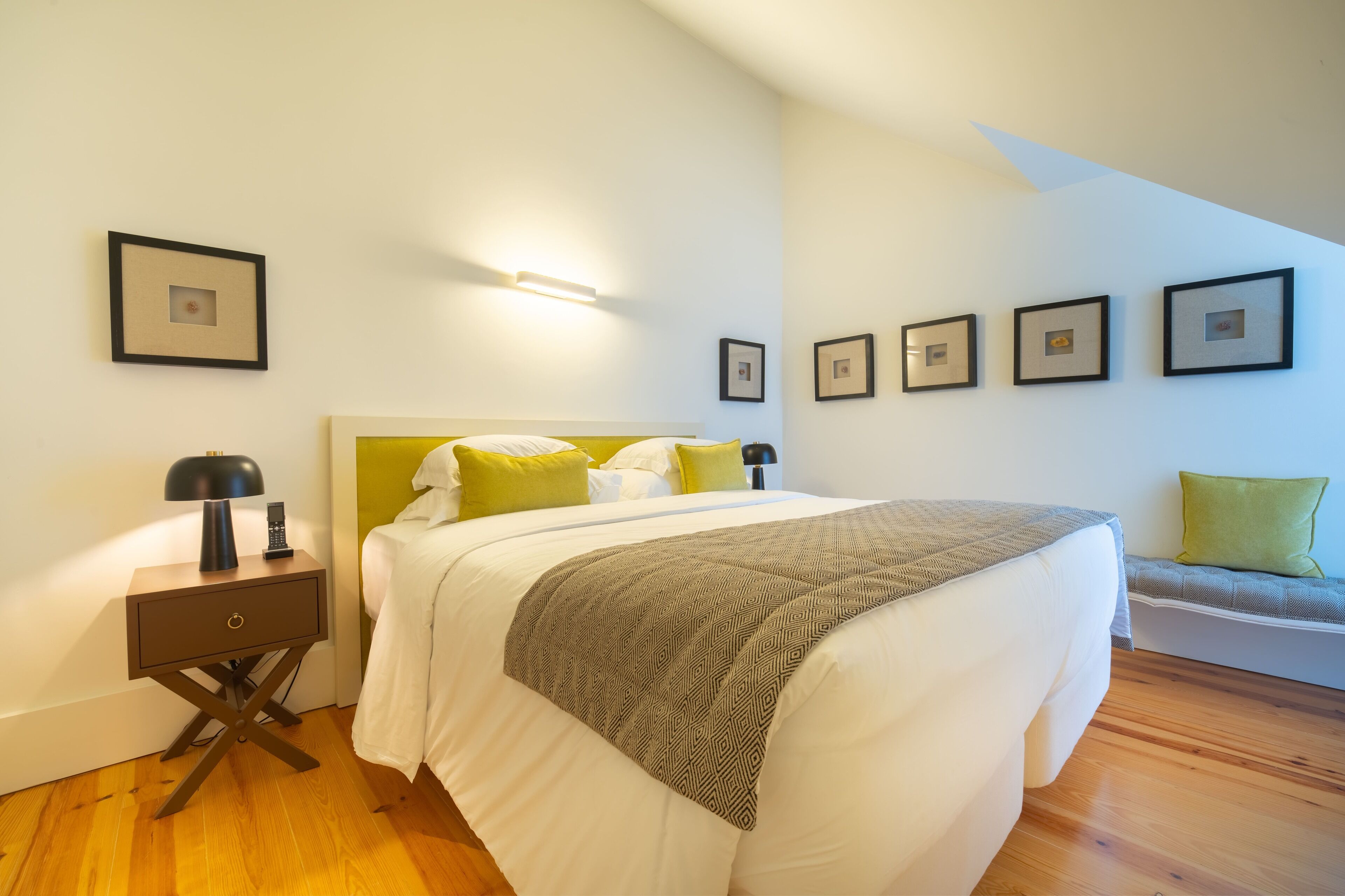 A bedroom with a bed, bedside table, lamp, and wall-mounted pictures.