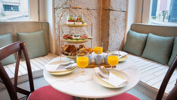 A breakfast setting with a three-tiered fruit and cheese board, a selection of pastries, and orange juice on a round table. - Once Upon Lisboa (Lisbon)