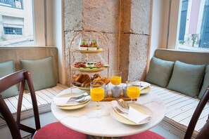 A breakfast setting with a three-tiered fruit and cheese board, a selection of pastries, and orange juice on a round table. - Once Upon Lisboa (Lisbon)