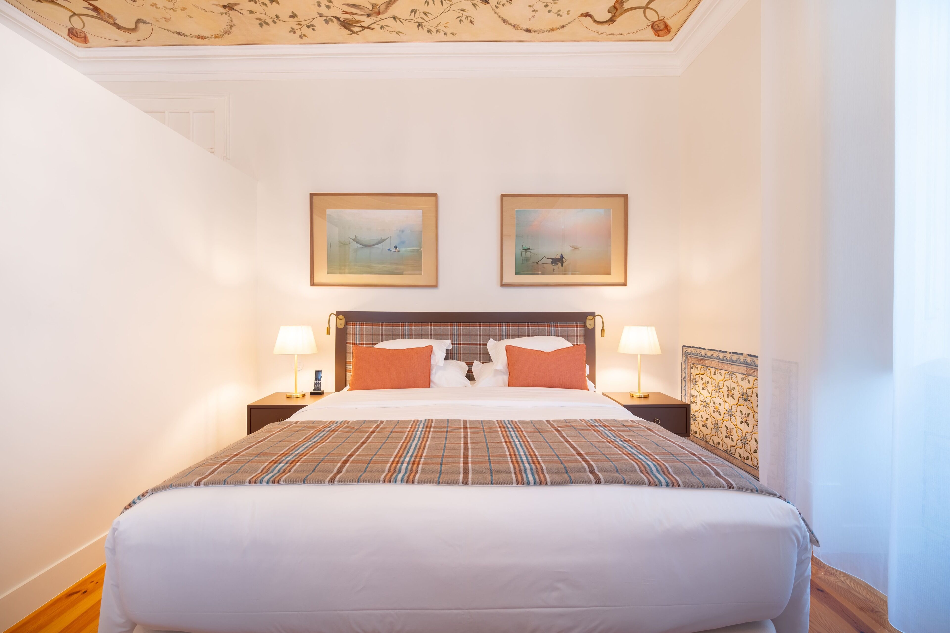 A hotel room with a large bed, two bedside tables with lamps, and two framed artworks on the wall.