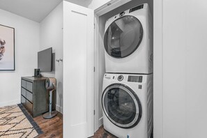 A laundry room with a stacked washer and dryer, a small cabinet, a fan, and a rug.