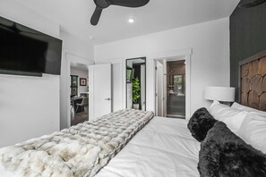 A modern hotel room with a large bed, a flat-screen TV mounted on the wall, and a ceiling fan.