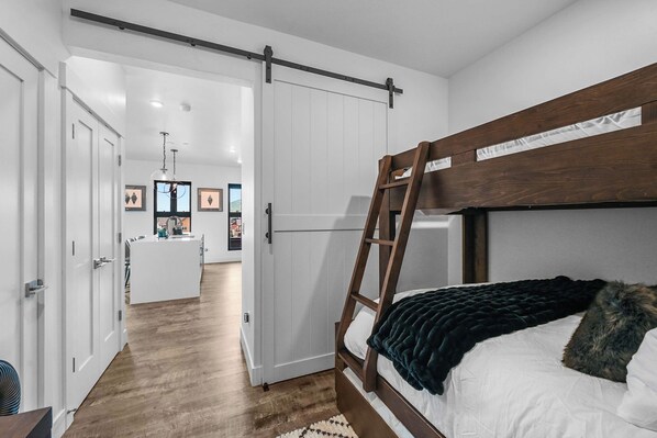 A bedroom with a bunk bed, a wooden ladder, a dark blanket, and a white door leading to a hallway.