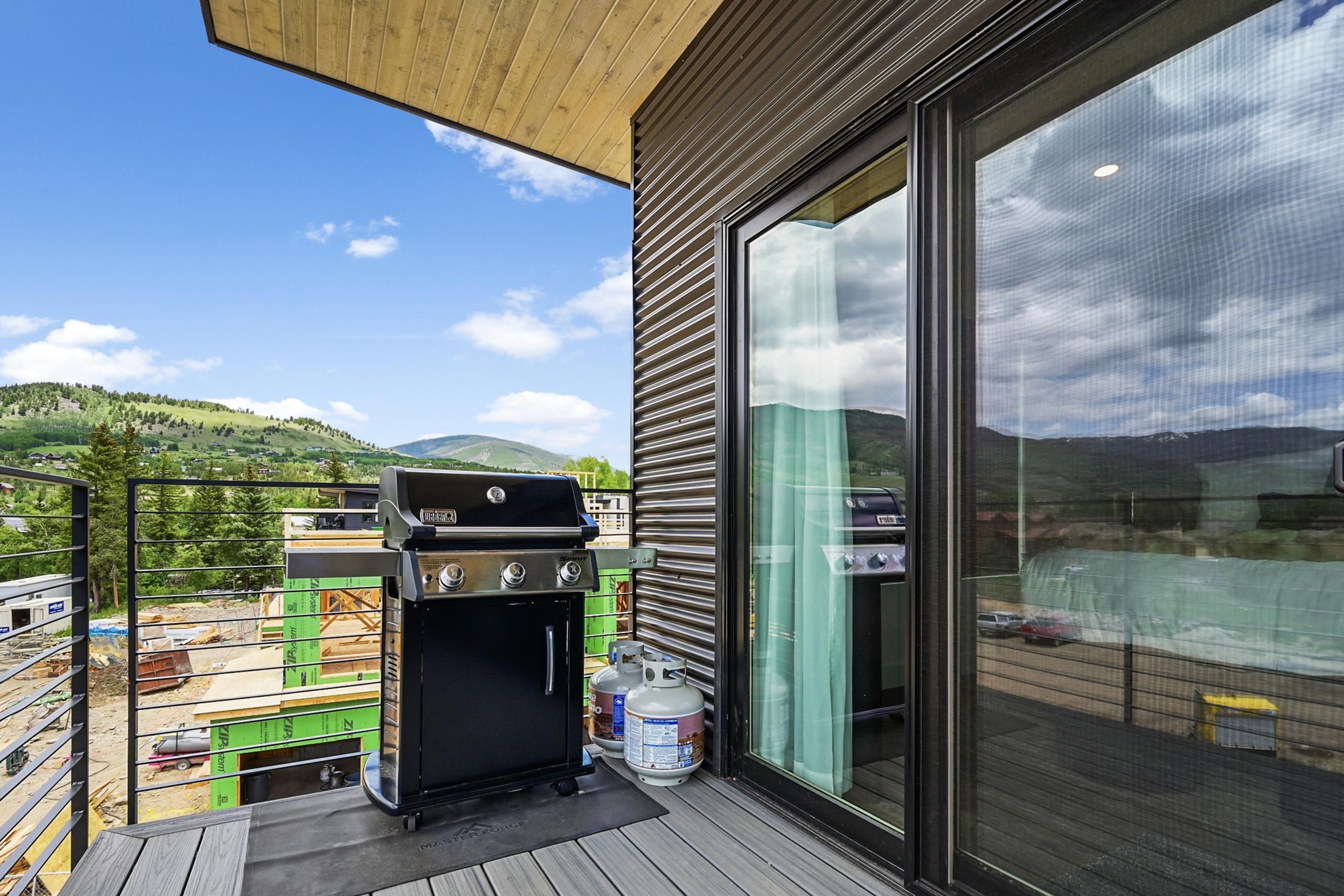 A balcony with a Weber Spirit grill, a large window, and a view of a hilly landscape.