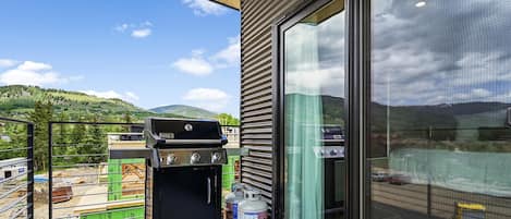 Un balcón con una parrilla Weber Spirit, un ventanal grande y vistas a un paisaje montañoso.