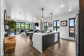 A modern kitchen with a large island, dark cabinetry, and pendant lighting.