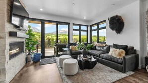 Ein modernes Wohnzimmer mit Kamin, Ledersofa und großen Fenstern mit Blick auf die Berge.