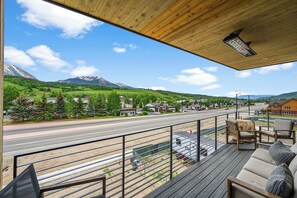 A wooden deck with outdoor seating overlooking a road and mountains.