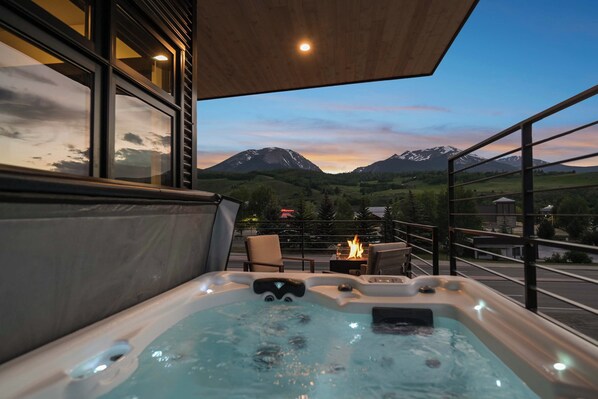 A hot tub with a mountain view, a chair, and a fire table.