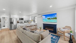 Una sala de estar moderna con un sofá, una chimenea y un televisor que muestra una escena de playa tropical.
