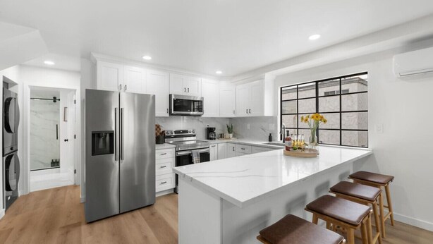 Una cocina moderna con muebles blancos, electrodomésticos de acero inoxidable y una isla grande con taburetes de bar.