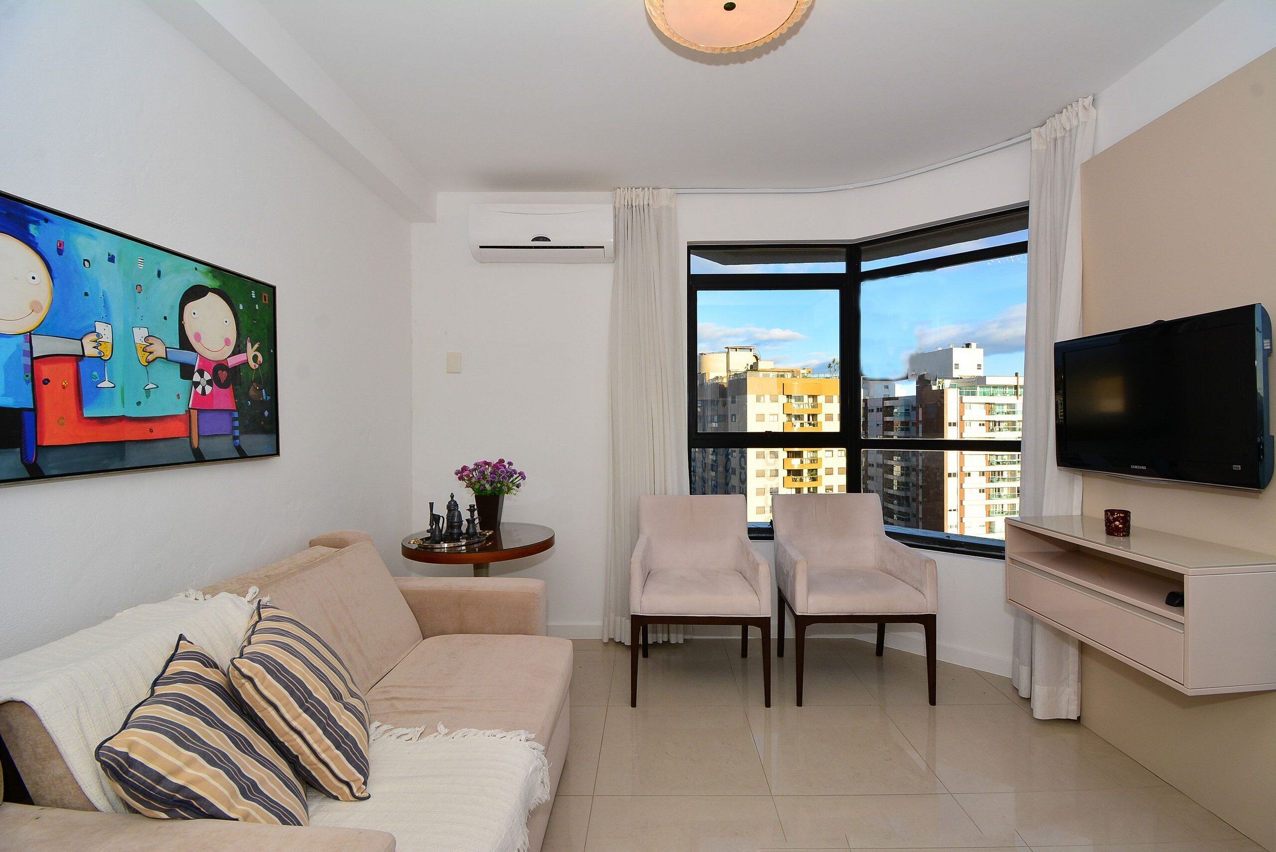 Un soggiorno moderno con un divano, due poltrone, una TV e un'ampia finestra con vista sulla città.