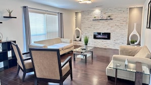 A modern living room with a sofa, armchairs, a coffee table, and a flat-screen TV mounted on a stone wall.