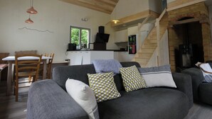 A cozy living room with a grey sofa, wooden ceiling, and a kitchen area in the background. - Eth Vergèr esvanit *** - vacation home 8 persons (Juzet-de-Luchon)