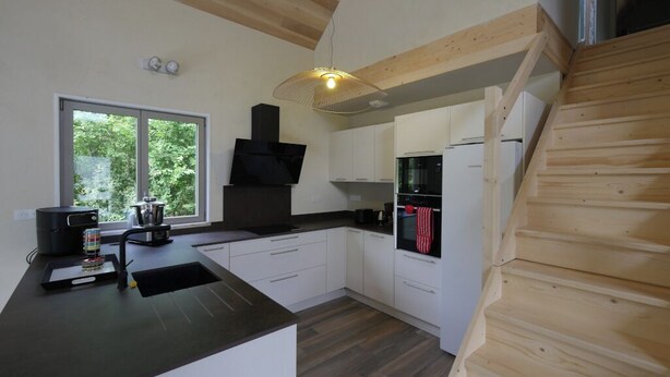 A modern kitchen with white cabinets, a black countertop, and a wooden staircase. - Eth Vergèr esvanit *** - vacation home 8 persons (Juzet-de-Luchon)