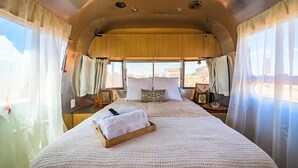 A cozy interior with a large bed, wooden headboard, and a view through the windows. - Airstream w/ Private Hot Tub (Unit G) - 4 Person Airstream with Private Hot Tub (Williams)