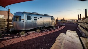 A silver RV parked in a driveway with a red canopy overhead. - Airstream w/ Private Hot Tub (Unit G) - 4 Person Airstream with Private Hot Tub (Williams)