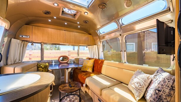 A cozy RV interior with a dining area, a sofa with cushions, and a TV mounted on the wall. - Airstream w/ Private Hot Tub (Unit G) - 4 Person Airstream with Private Hot Tub (Williams)