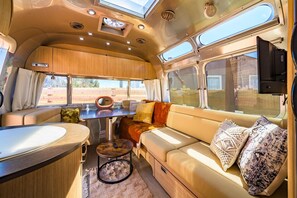 Ein gemütliches Wohnmobil-Interieur mit Essbereich, einer Couch mit Kissen und einem an der Wand befestigten Fernseher.