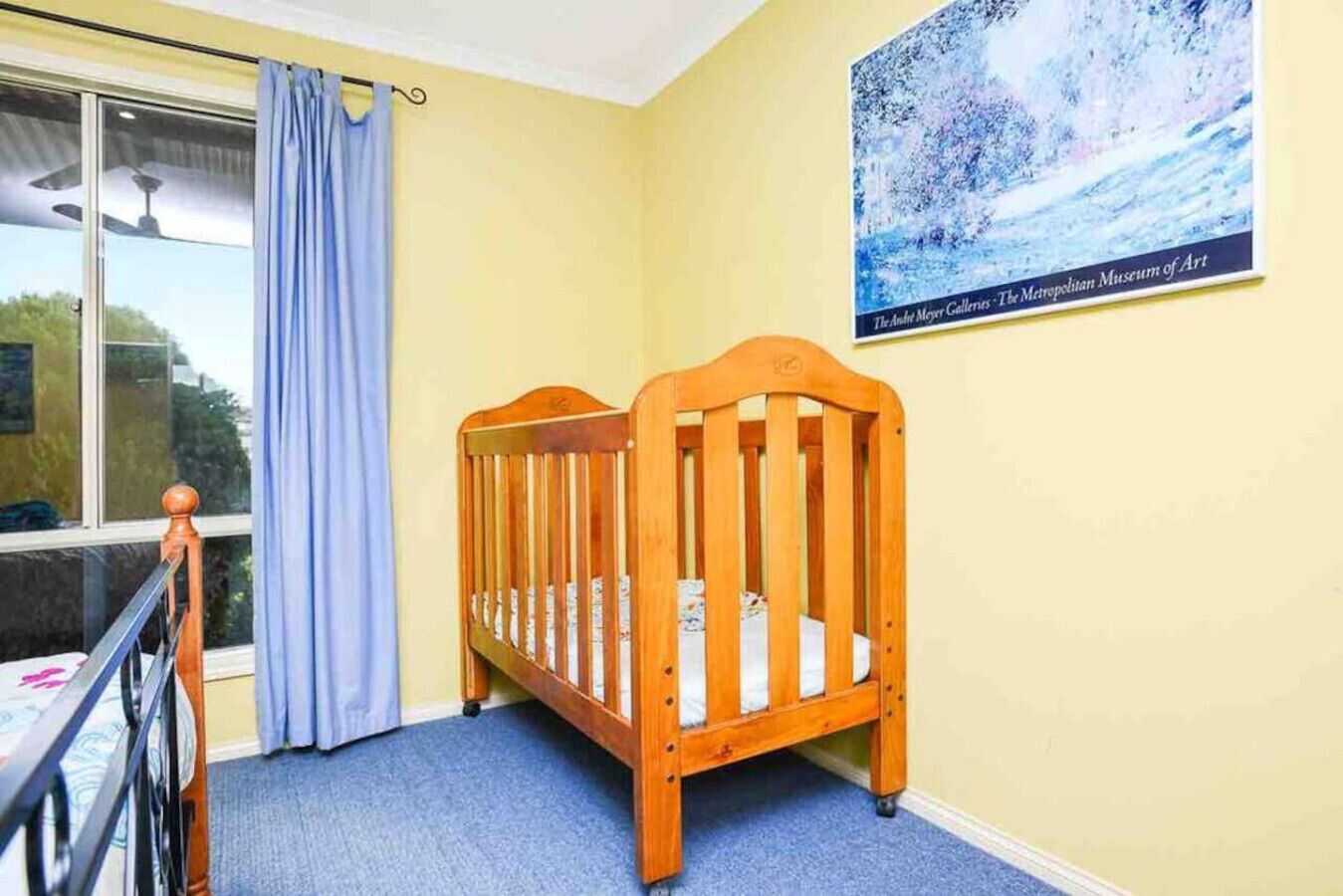 A room with a wooden crib, a window with a view, and a painting on the wall.