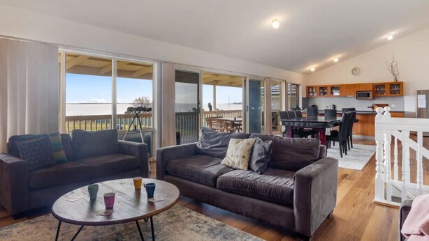 A spacious living area with a large sofa, a coffee table, and a balcony with a view. - Hindmarsh Hideaway-—Waterfront Pet-friendly Living (Hindmarsh Island)