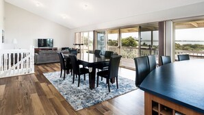 A modern dining area with a large table and chairs, a kitchen area with a TV, and a balcony with a view. - Hindmarsh Hideaway-—Waterfront Pet-friendly Living (Hindmarsh Island)