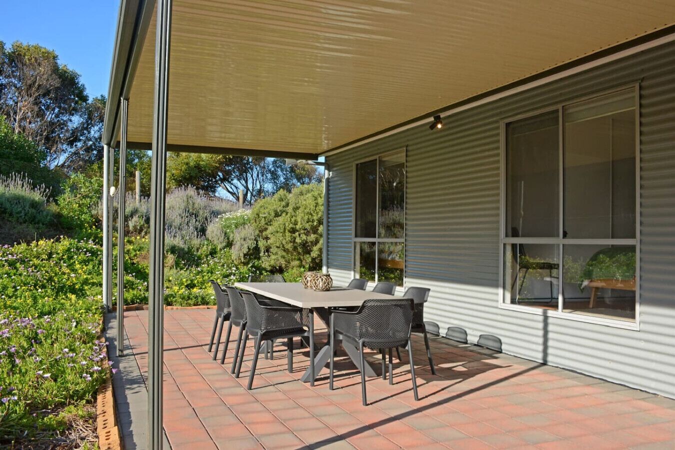 A covered patio with a table and chairs, surrounded by a garden.