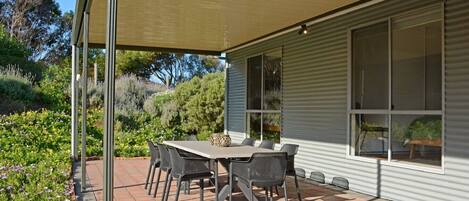A covered patio with a table and chairs, surrounded by a garden.