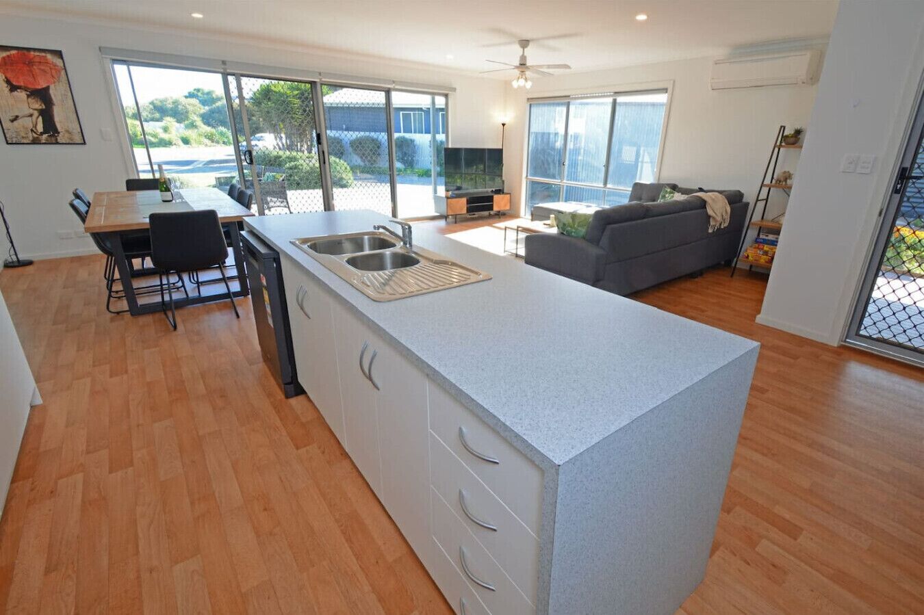 A modern kitchen with a large island, dining area, and a living space with a sofa and TV.